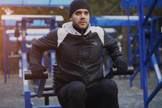 Attractive young man doing exercise in outdoor gym in winter park